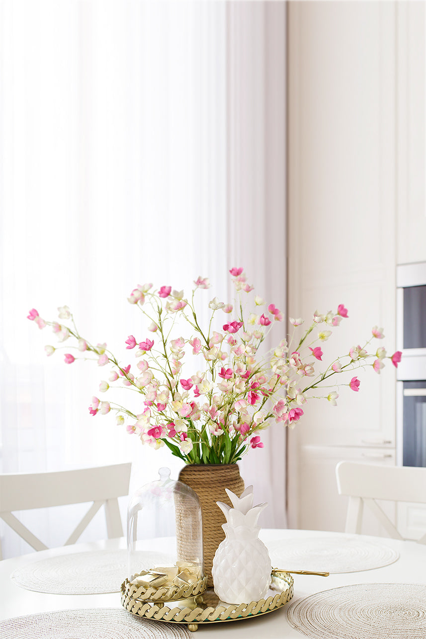 Vibrant pink faux Enkianthus blooms exude grace and charm, nestled in a fabric vase atop a dining table for a delightful centerpiece.