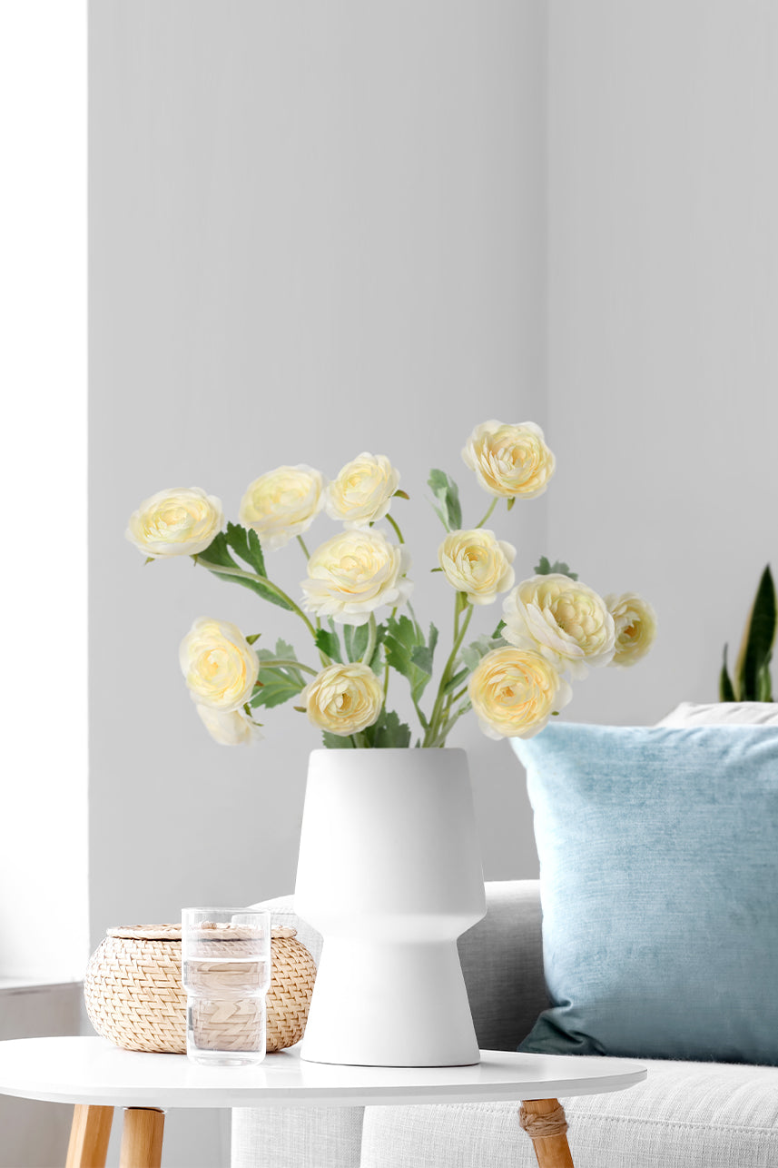 A lovely display of yellow peach faux Ranunculus flower branches, elegantly arranged within a white vase for a touch of timeless beauty.