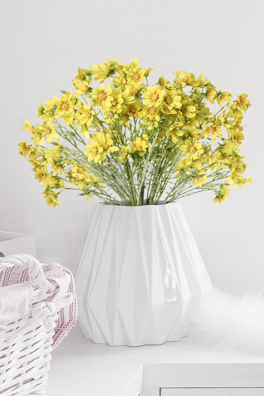 Sunny yellow artificial faux Cosmos flower blooms bring a burst of joy to home decor, elegantly displayed in a white vase for a touch of timeless beauty.