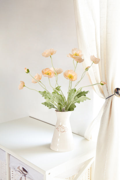 Create a soothing atmosphere in your bedroom with the vibrant allure of coral pink fake Papaver Rhoeas flowers displayed on a bedside table by the window.