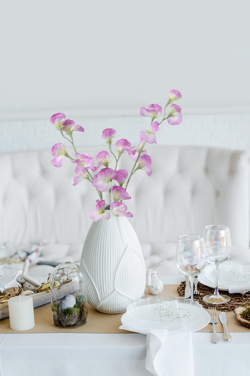 Artificial purple lathyrus odoratus flowers were placed in a white ceramic vase, tableware and candles were placed on the table.