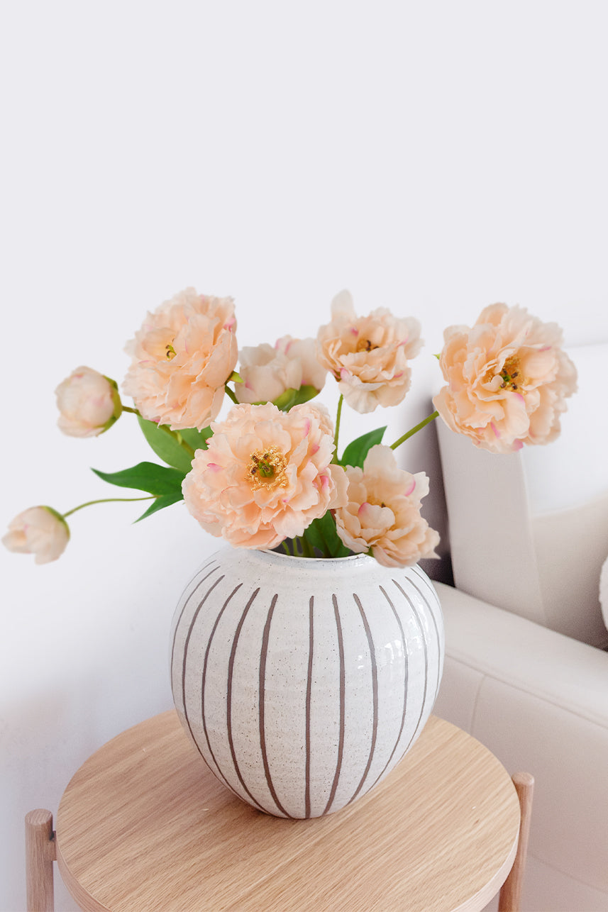 Peach artificial peonies are placed in a white striped ceramic vase, which you can place on the table next to the sofa.