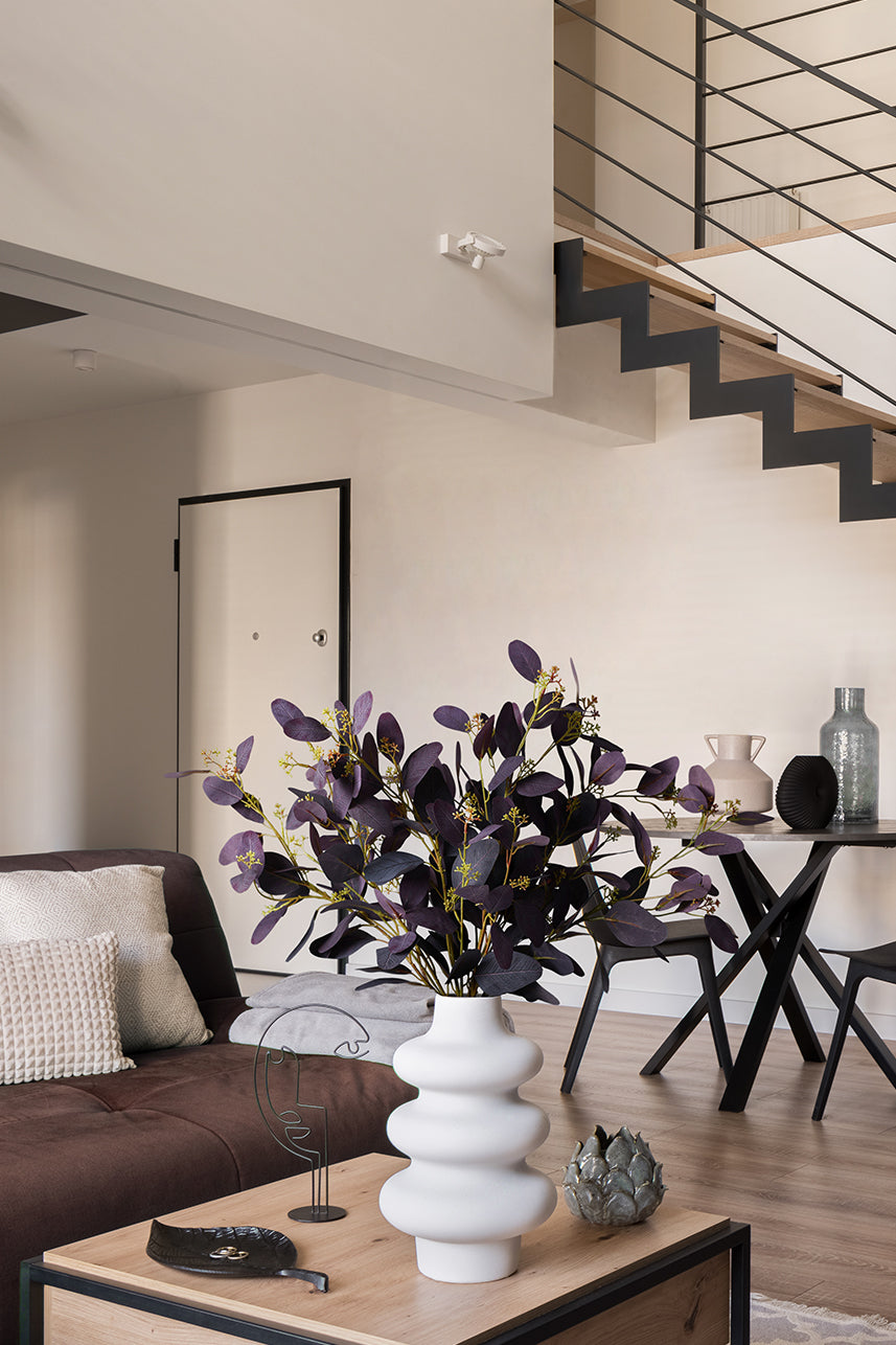 A white vase with burgundy Parisian eucalyptus leaves on the coffee table is perfect for a brown-toned home decor.