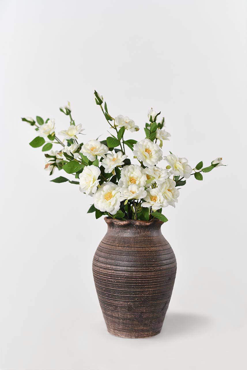 The budding to full bloom artificial cream-white Iceberg Rose flowers are complete with a textured vase perfect as a centerpiece.