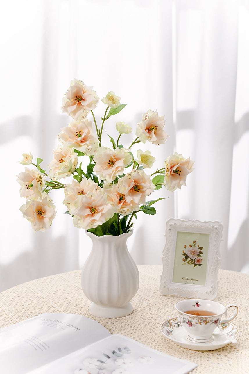 Sunlight spilled through the curtains throughout the room, and artificial blush peach clematis were placed in a white vase, becoming a floral arrangement artwork.