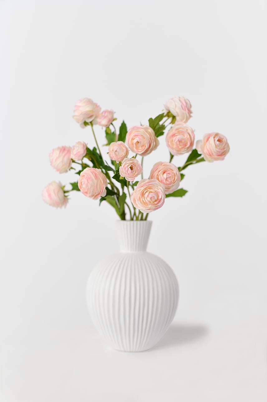 Artificial silk flowers in light pink with bright green leaves arranged in a white vase, creating a blooming effect