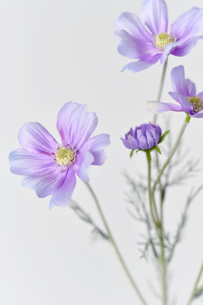A close-up of the light purple Faux Cosmos flowers with yellow centers and softly curved petals.