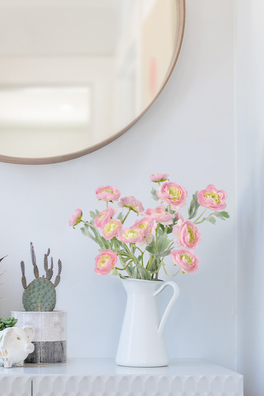 Artificial pink mauve ranunculus are placed in a white vase, which you can place in a prominent place, such as on a coffee table or shelf.
