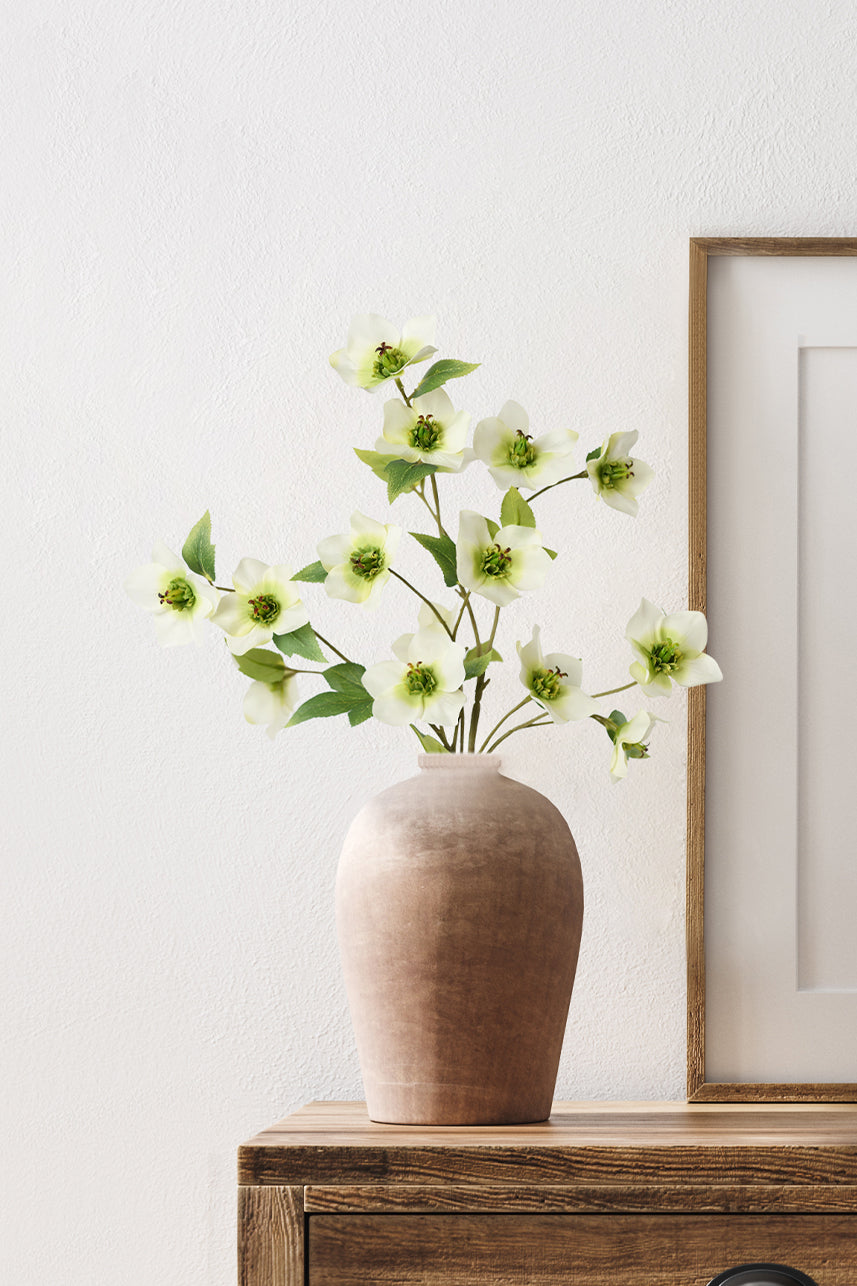 The artificial helleborus inserted into the brown ceramic vase fit perfectly into the wooden tone of the home scene.
