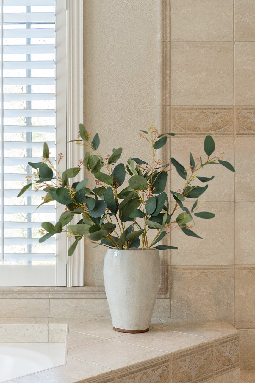 Lush green artificial Parisian Eucalyptus leaves elegantly arranged in a white vase, creating a refreshing and inviting ambiance.