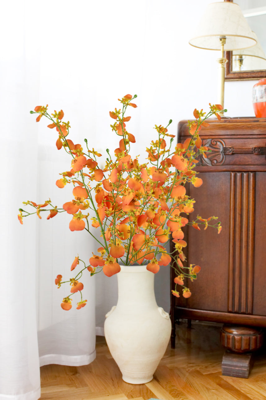 Enchanting orange Dancing Orchid artificial flowers sway gracefully in a white ceramic vase, adorning the bedroom with their vibrant allure.