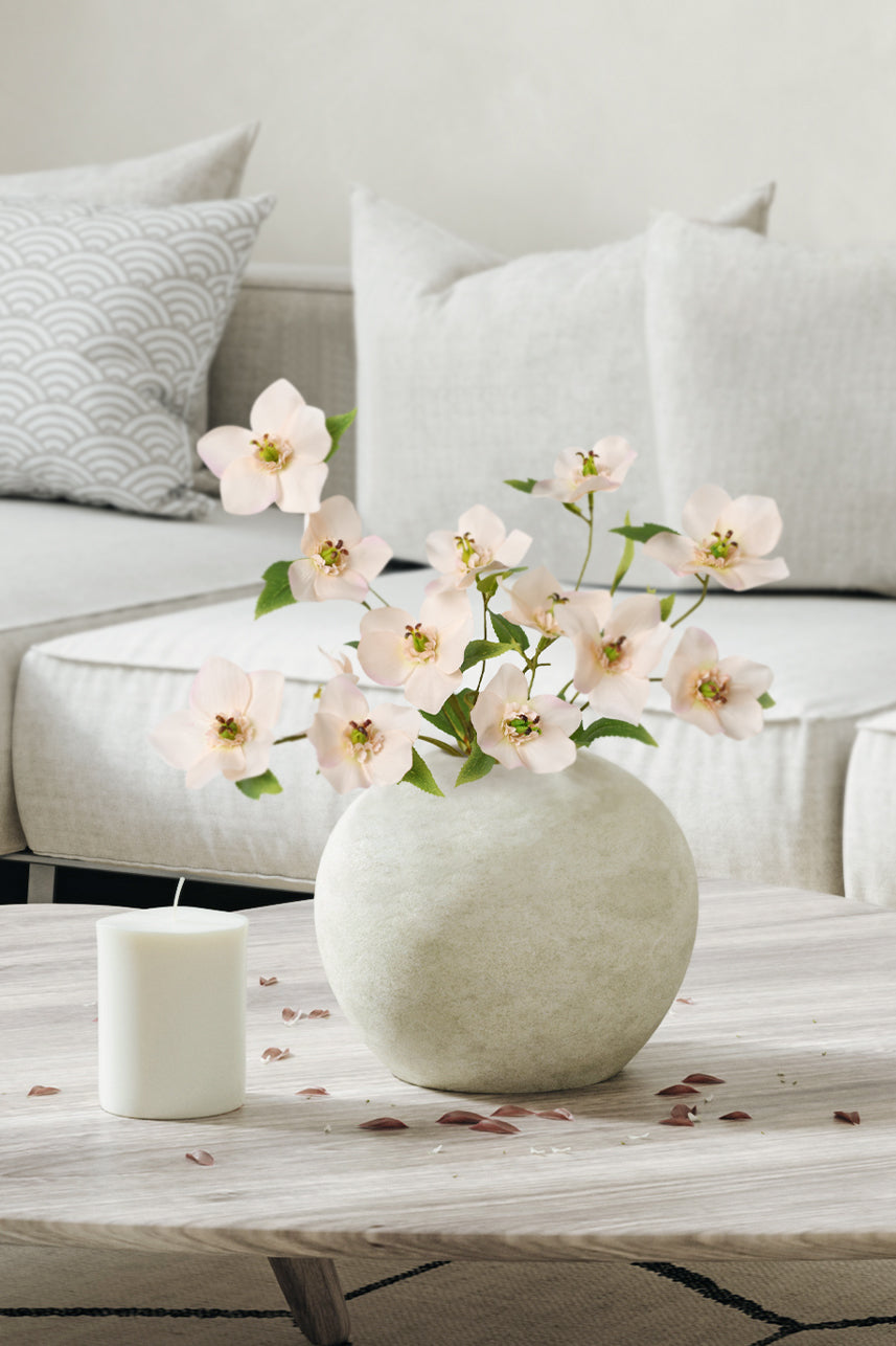 Peach pink artificial Helleborus blossoms create a stunning display in a ceramic vase, enhancing the living room decor with their delicate beauty and grace.