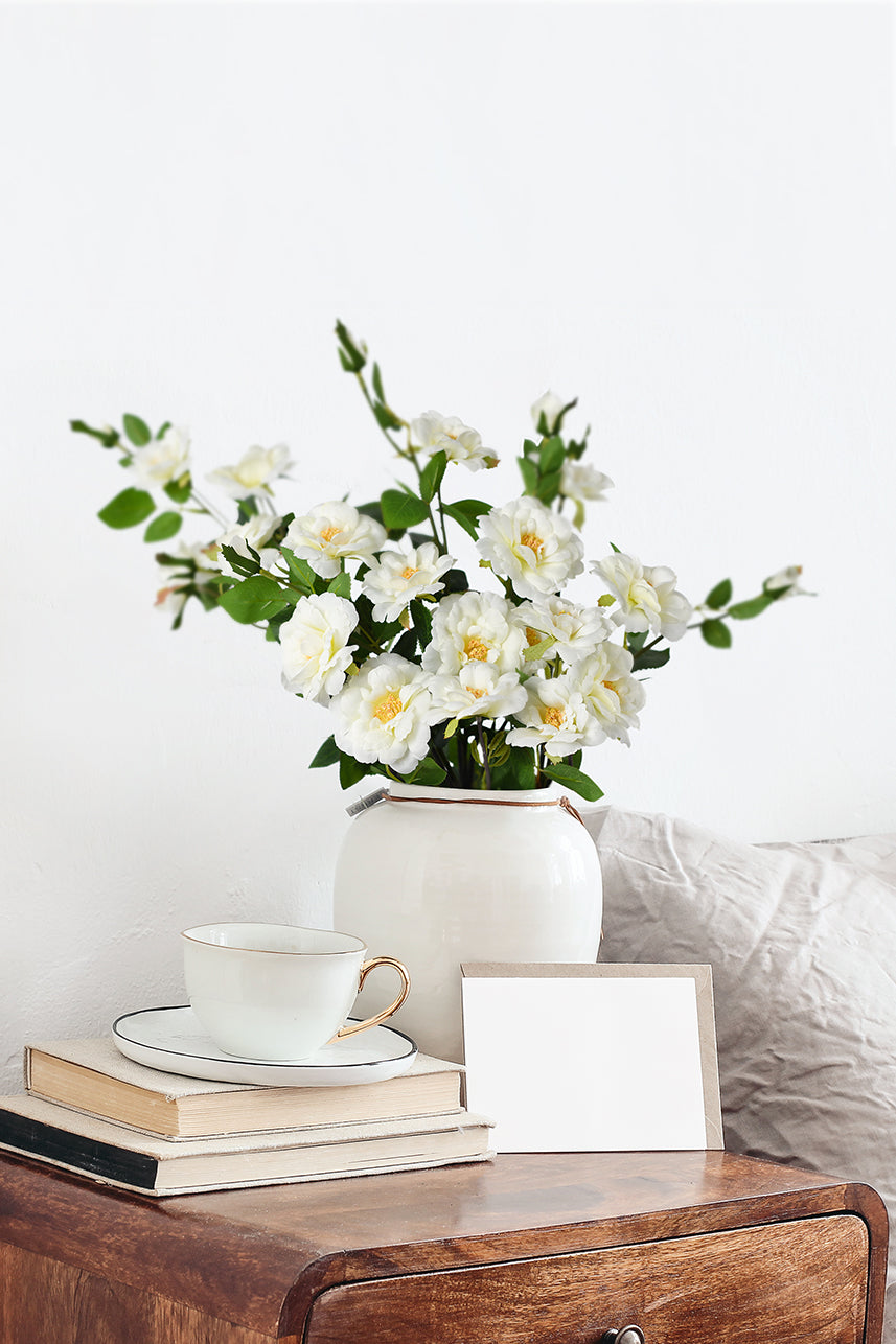 Enhance your bedside desk with the delicate charm of an artificial cream white Iceberg Rose flower, creating a serene and beautiful decor.