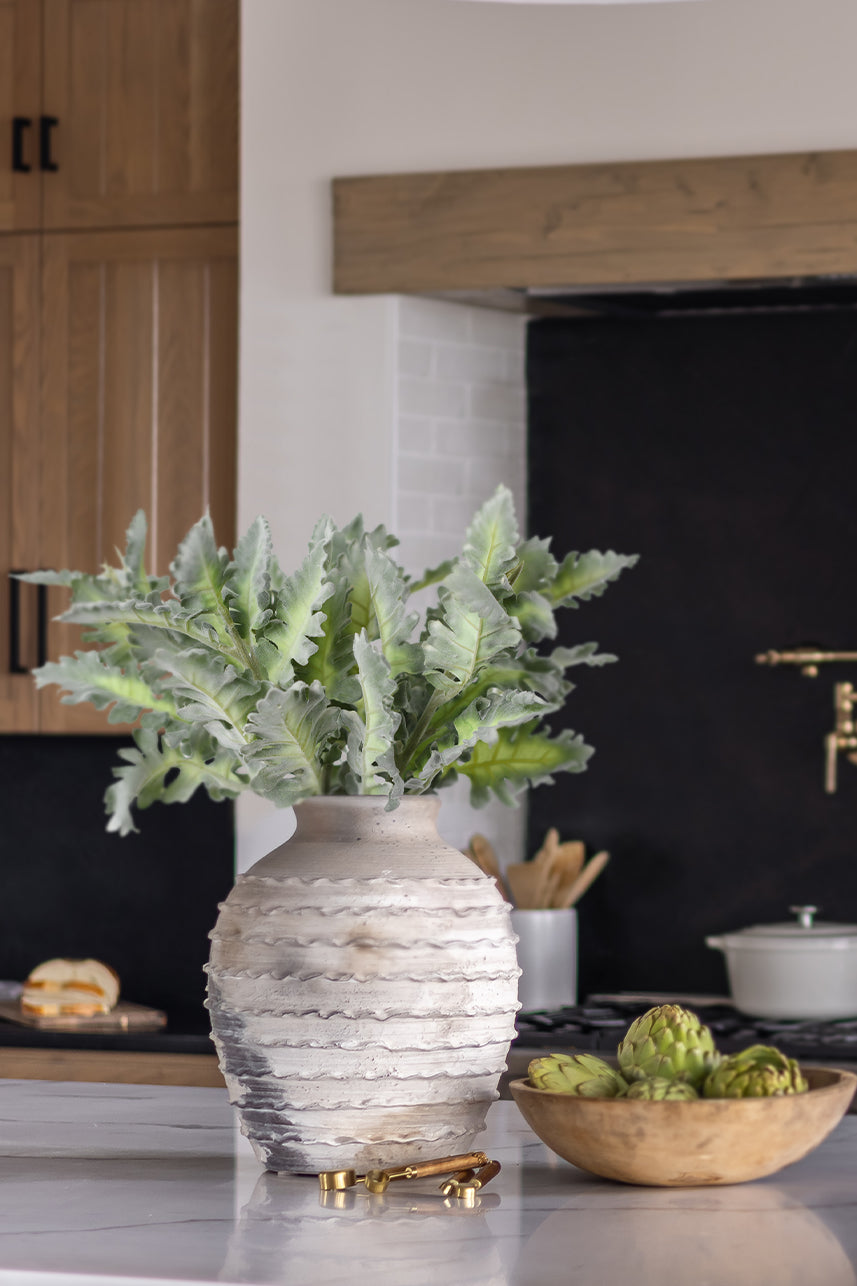 Decorating the dining table, faux Senecio Cineraria in vibrant green delights in a ceramic vase, bringing a touch of natural beauty to the setting.