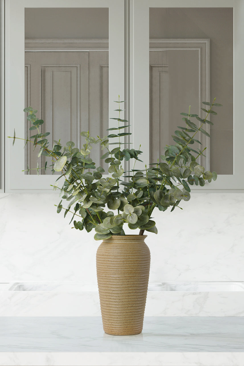 Artificial spiral eucalyptus leaves stretch naturally in a brown vase, blending well with the modern style of the home.