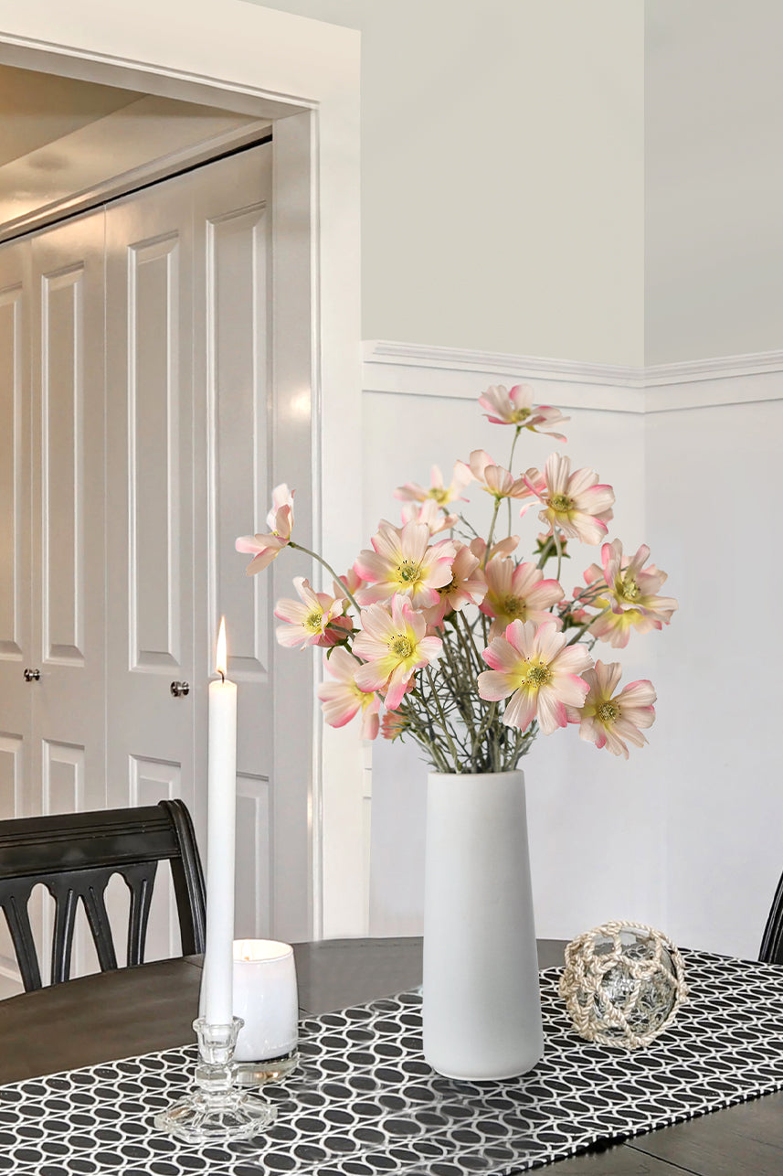 Vases filled with blush pink cosmos were placed on a simple dining table with candles next to the vases. This faux flower arrangement is perfect for home decor.