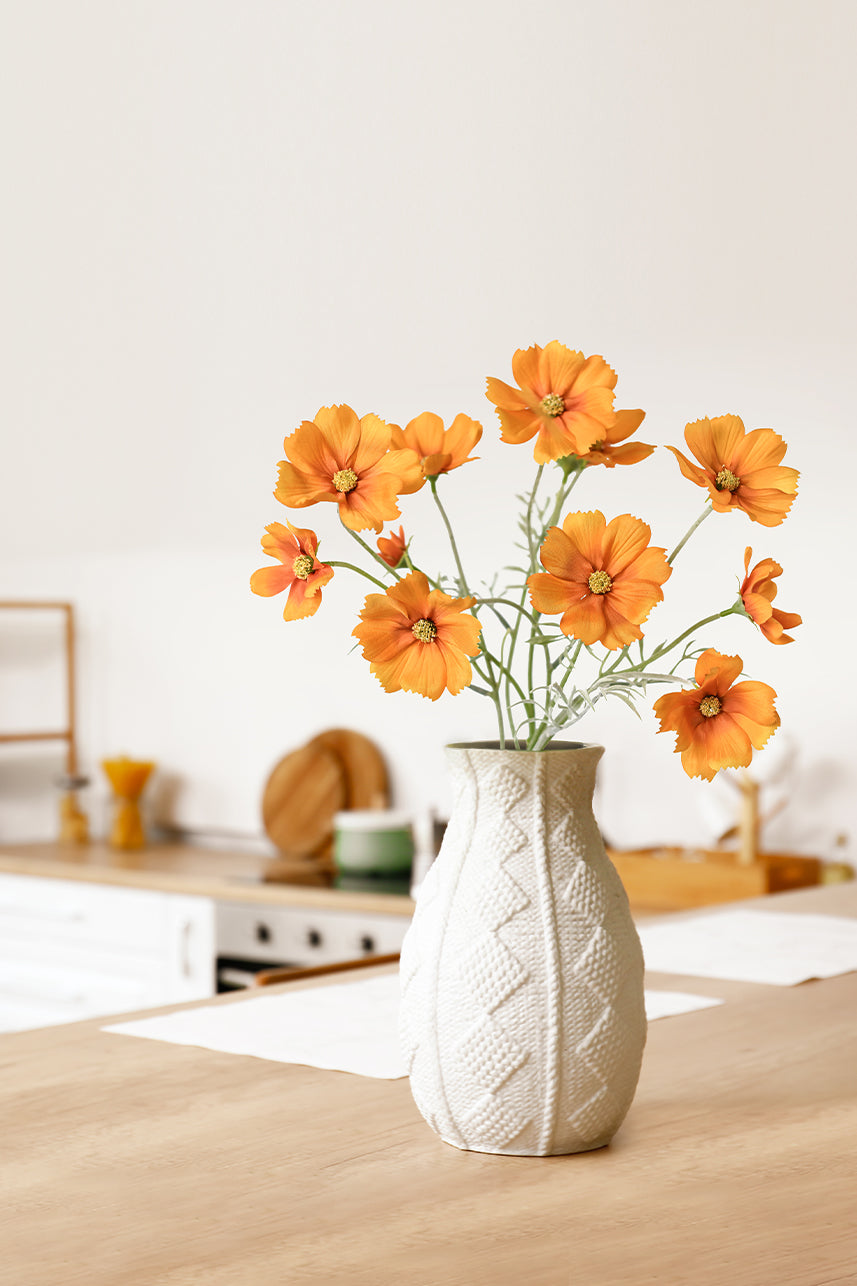The floral vase in the living room contains orange cosmos bipinnatus flowers, a bright orange color that accents the wood tone of the home.