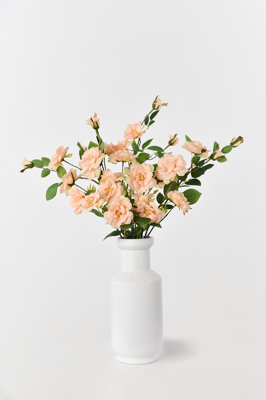 An elegant centerpiece vase filled with peach-colored artificial Iceberg roses with lifelike petals, perfect for home decor or special events.