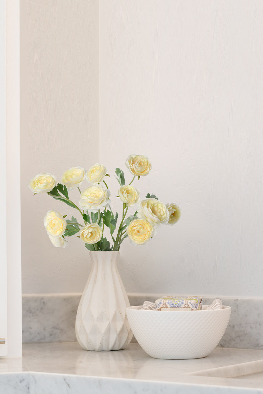 The yellow peach artificial ranunculus seem to be more suitable for a warm and cozy home setting, and the insertion of a white vase makes it a good floral arrangement.