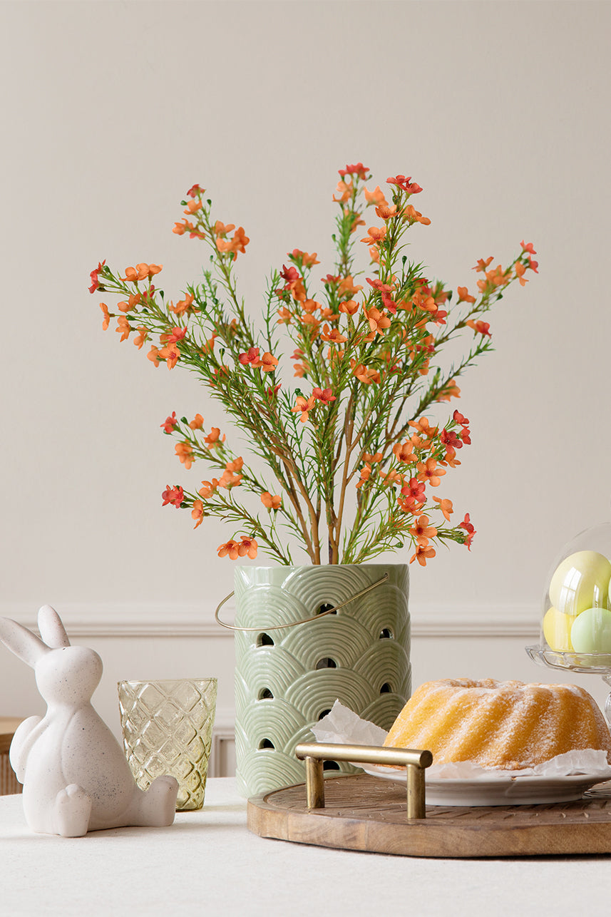 The orange artificial wax flowers in the vase are particularly conspicuous. Next to the vase are some food.