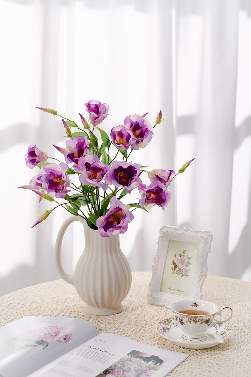 Faux flower petals in full bloom, white vase filled with fake flowers suitable for placing in a warm scene, the table with tea cups, photo frames and magazines.