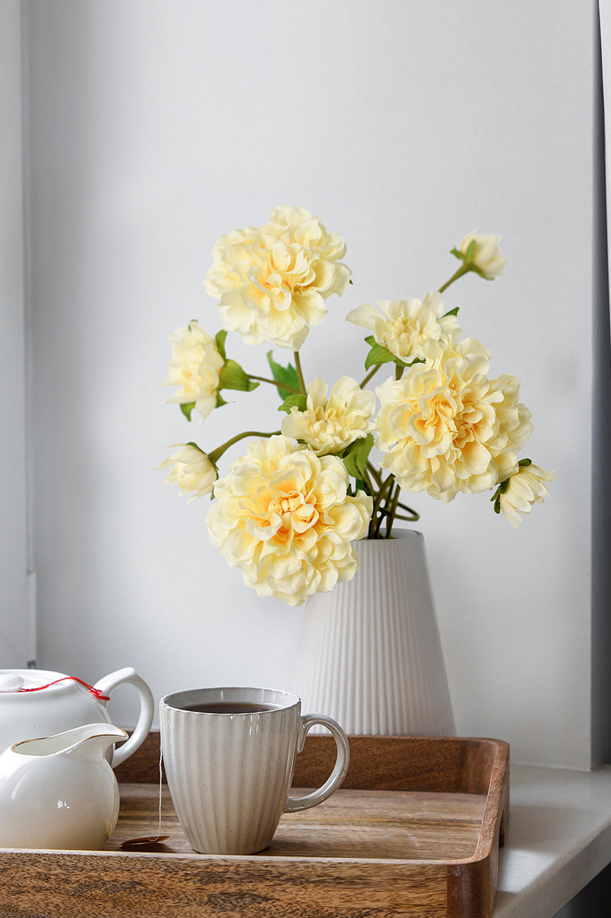 Artificial yellow peach paeonia with a white vase, giving a natural and comfortable feeling, with a tea cup next to the vase.