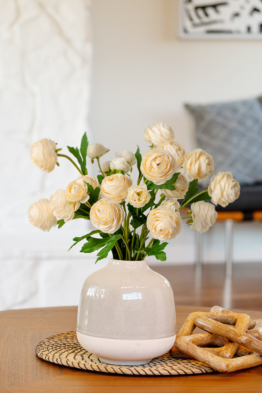 The yellow peach artificial ranunculus were placed in a light-colored vase and this floral arrangement was placed on the dining table.